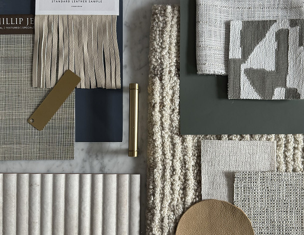 A flat lay of fabric, leather, and material swatches in neutral tones, along with a brass handle and a color sample on a marble surface.