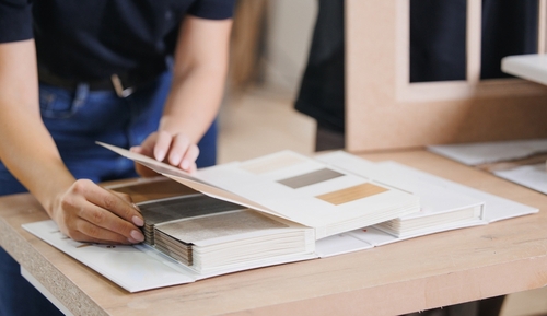 A person opens a sample book displaying various wood and laminate finishes on a table.