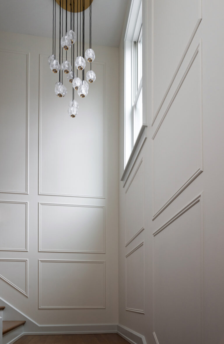A modern staircase with white paneled walls, a large window, and a hanging chandelier with multiple glass globe lights.